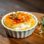 A golden-brown crab brulee with caramelized top served in a ramekin.